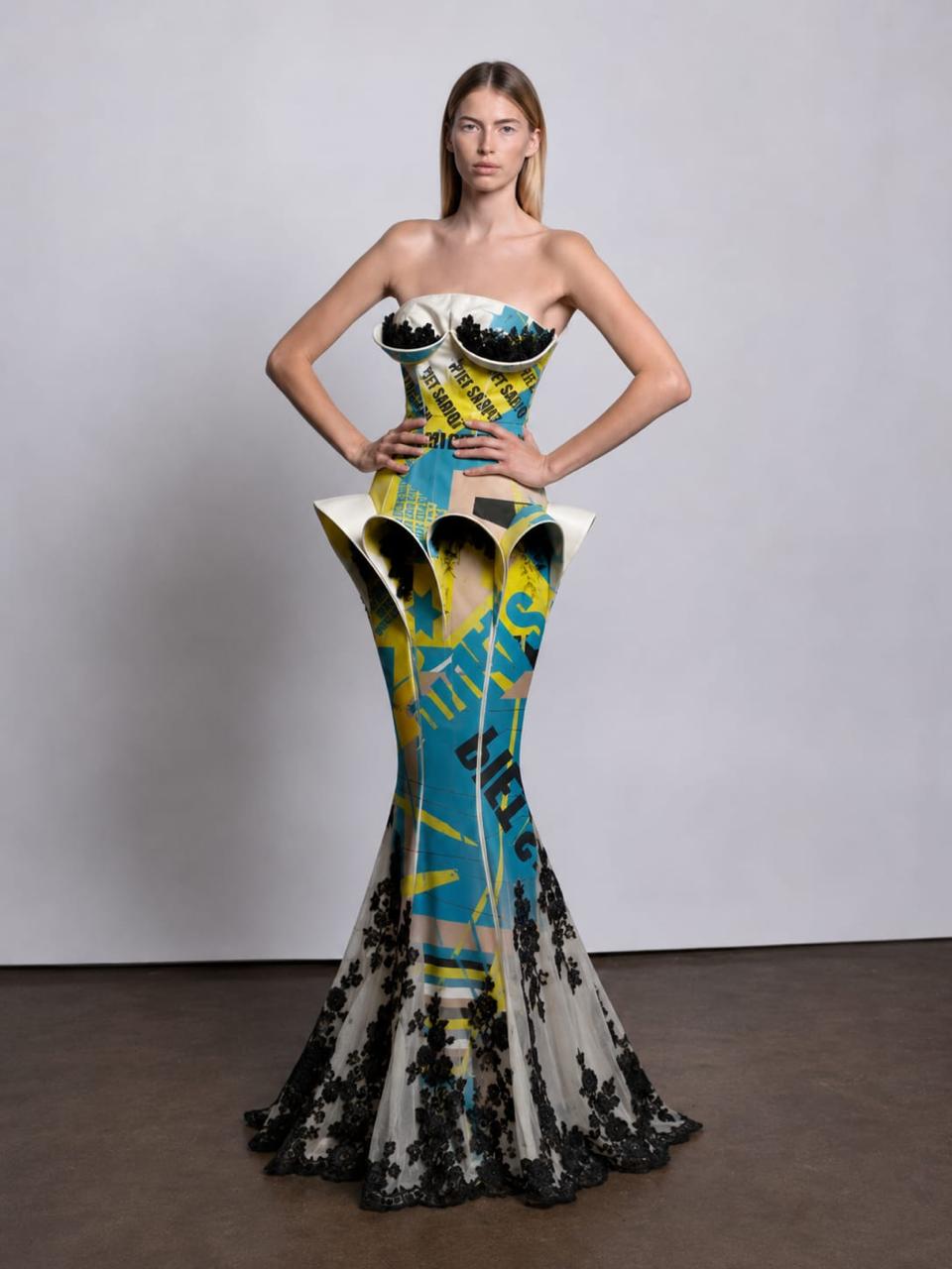 strapless mermaid gown with a sculptural corset-style bodice and flared skirt. The dress has a bold abstract print in turquoise, yellow, black, and off-white, with black lace at the hem.
