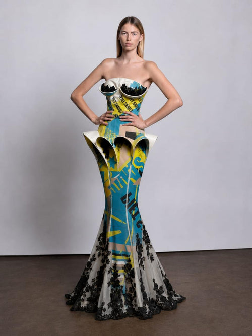 strapless mermaid gown with a sculptural corset-style bodice and flared skirt. The dress has a bold abstract print in turquoise, yellow, black, and off-white, with black lace at the hem.