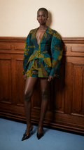 Mini jacket and matching mini skirt in a teal and mustard yellow graphic print, paired with black pointed-toe heels.
